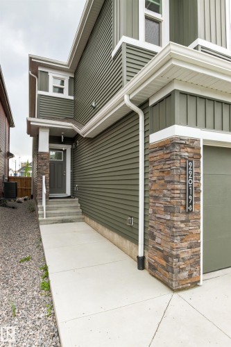 Siding exterior with stone accents, covered entry, front door with window inset, white window trim, and concrete pathway - 22019 82 Avenue Nw, Edmonton, AB - Outdoor