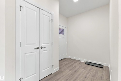 Entryway featuring wood-finish flooring, a white paneled entry door with frosted glass, and white bi-fold closet doors with brushed nickel hardware - 22019 82 Avenue Nw, Edmonton, AB - Indoor Photo Showing Other Room