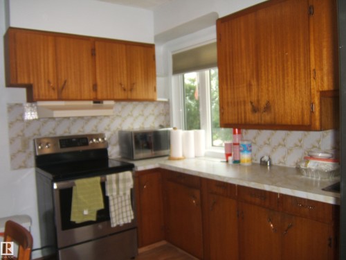 Warm wood cabinetry and stainless steel appliances anchor this kitchen, featuring ceramic tile backsplash, laminate countertops, and a black electric range - 4809 47A Street, Two Hills, AB - Indoor Photo Showing Kitchen