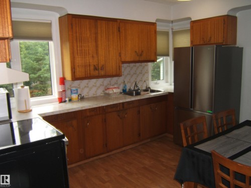 Wood-finish flooring with full kitchen cabinetry, white countertop, and stainless steel refrigerator - 4809 47A Street, Two Hills, AB - Indoor Photo Showing Kitchen
