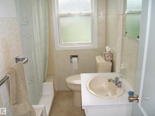 Bathroom featuring ceramic tile walls, a round pedestal sink with chrome faucet, toilet with wall-mounted tank, and a window with frosted glass for natural light and privacy - 4809 47A Street, Two Hills, AB - Indoor Photo Showing Bathroom