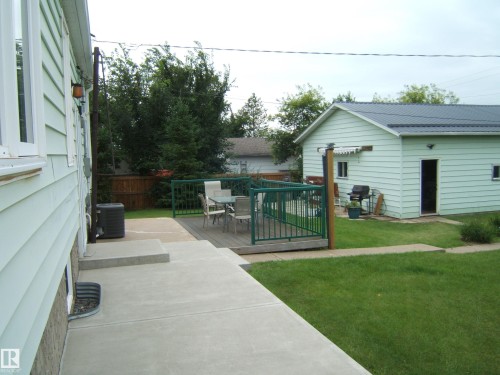 Spacious backyard with mature landscaping, concrete patio, composite deck with metal railings, detached outbuilding, and manicured lawn—ideal for outdoor entertaining and recreation - 4809 47A Street, Two Hills, AB - Outdoor With Exterior