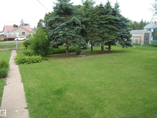 Expansive manicured lawn with mature shade trees and established landscaping - 4809 47A Street, Two Hills, AB - Outdoor