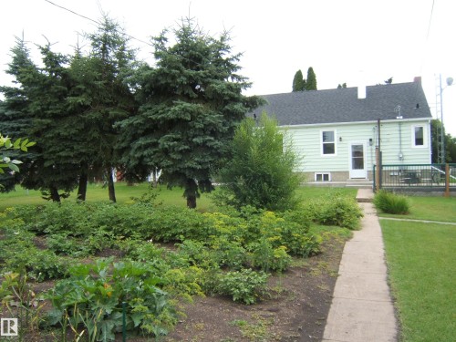 Charming ranch-style home set on a landscaped lot featuring mature shade trees, established garden beds with mixed plantings, and a manicured lawn - 4809 47A Street, Two Hills, AB - Outdoor