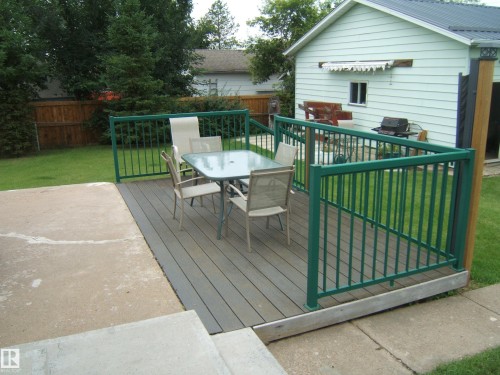 Composite deck featuring composite decking with black metal railing, integrated seating area with dining table and chairs, and mature landscaping with established trees and manicured lawn - 4809 47A Street, Two Hills, AB - Outdoor With Deck Patio Veranda With Exterior