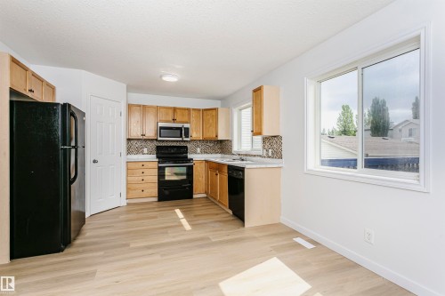 Kitchen with light wood-finish cabinetry, black appliances, mosaic tile backsplash, and light wood-finish flooring - 37 Suntree Promenade, Leduc, AB - Indoor Photo Showing Kitchen