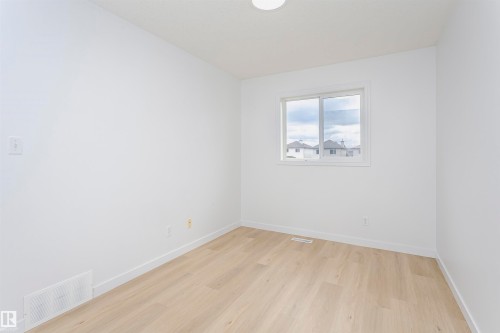 Bright secondary bedroom featuring light wood-finish flooring, white painted walls, and a large window with natural light and exterior views - 37 Suntree Promenade, Leduc, AB - Indoor Photo Showing Other Room