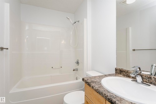 Bathtub with integrated shower, single vanity with oval sink, wood-finish cabinetry, and speckled countertop - 37 Suntree Promenade, Leduc, AB - Indoor Photo Showing Bathroom