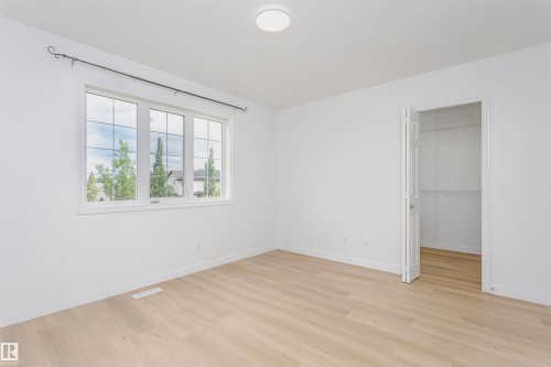 Spacious room with wood-finish flooring, a large window with grid panes, and a closet with bifold doors - 37 Suntree Promenade, Leduc, AB - Indoor Photo Showing Other Room