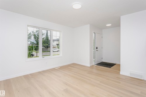 Light wood-finish flooring, white walls, large window with grid panes, recessed ceiling lights, and a white entry door - 37 Suntree Promenade, Leduc, AB - Indoor Photo Showing Other Room