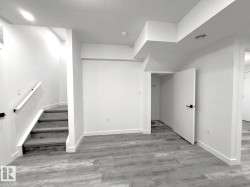 Wood-finish flooring, white walls, and a staircase with a white handrail - 