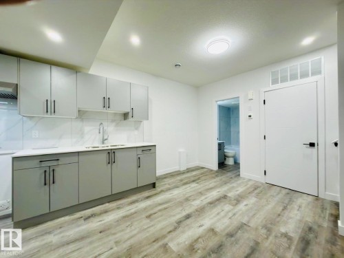 Kitchenette featuring gray shaker-style cabinetry, white countertops, a stainless steel sink with a gooseneck faucet, and wood-finish flooring - 1312 35 Street Nw, Edmonton, AB 