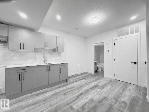 Contemporary kitchen featuring shaker-style cabinetry, quartz countertops, a double basin sink, and a tiled backsplash - 1312 35 Street Nw, Edmonton, AB 