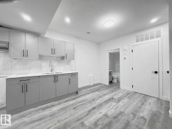 Contemporary kitchen featuring shaker-style cabinetry, quartz countertops, a double basin sink, and a tiled backsplash - 