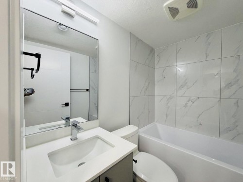 Modern bathroom featuring a rectangular vanity sink with a chrome faucet, a full-width wall mirror, and a white bathtub surrounded by white marble-look tile - 1312 35 Street Nw, Edmonton, AB 