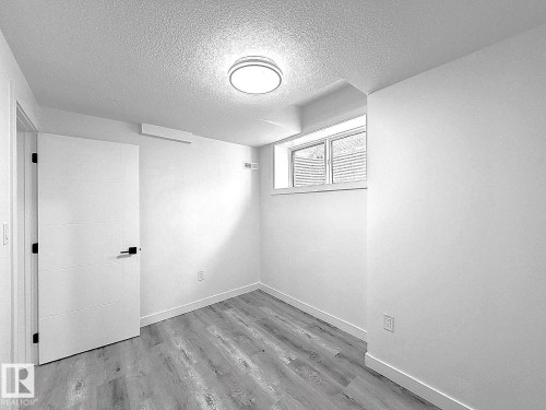 Neutral wall paint, recessed window, wood-finish flooring, overhead flush-mount lighting, and a paneled door with dark hardware - 1312 35 Street Nw, Edmonton, AB 