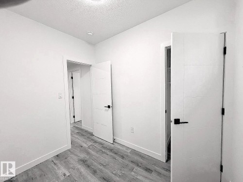 Wood-finish flooring with white baseboards, recessed ceiling lighting, and modern white doors with black hardware - 1312 35 Street Nw, Edmonton, AB 