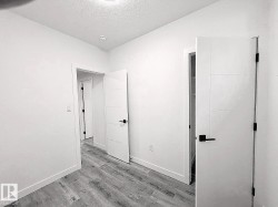 Wood-finish flooring with white baseboards, recessed ceiling lighting, and modern white doors with black hardware - 