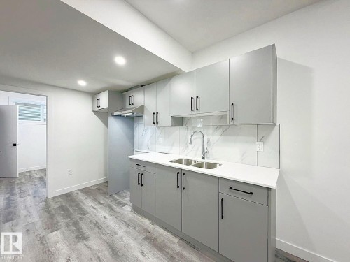 Kitchen featuring light gray cabinetry, white countertops, stainless steel dual basin sink, stainless steel range hood, and wood-finish flooring - 1312 35 Street Nw, Edmonton, AB 