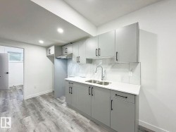 Kitchen featuring light gray cabinetry, white countertops, stainless steel dual basin sink, stainless steel range hood, and wood-finish flooring - 