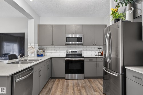 Well-appointed kitchen featuring wood-finish flooring, grey cabinetry, stainless steel appliances, white subway tile backsplash, and light-toned countertops - 17 Spruce Ridge Cove, Spruce Grove, AB - Indoor Photo Showing Kitchen With Double Sink With Upgraded Kitchen