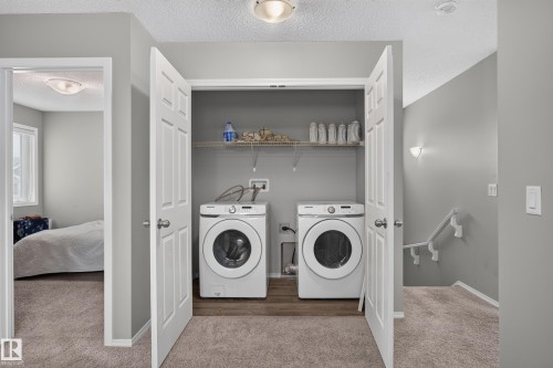 Laundry closet with wood-finish flooring, equipped with a front-load washer and dryer, and an overhead wire shelf - 17 Spruce Ridge Cove, Spruce Grove, AB - Indoor Photo Showing Laundry Room