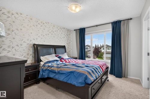 Window with exterior neighborhood visibility, neutral tone carpeting, ceiling-mounted light fixture, and a wall with decorative wallpaper - 17 Spruce Ridge Cove, Spruce Grove, AB - Indoor Photo Showing Bedroom
