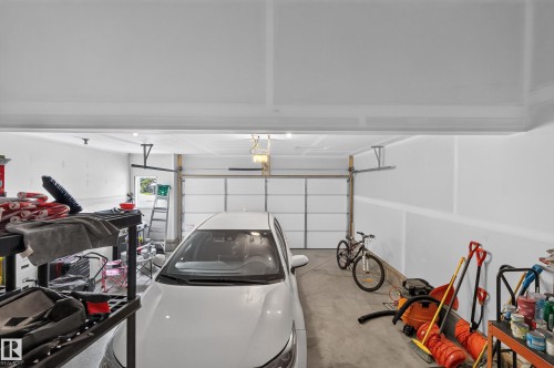 Spacious garage featuring epoxy-coated flooring, overhead storage systems, pendant lighting, and ample room for vehicles and recreational equipment including bicycles and tools - 17 Spruce Ridge Cove, Spruce Grove, AB - Indoor Photo Showing Garage