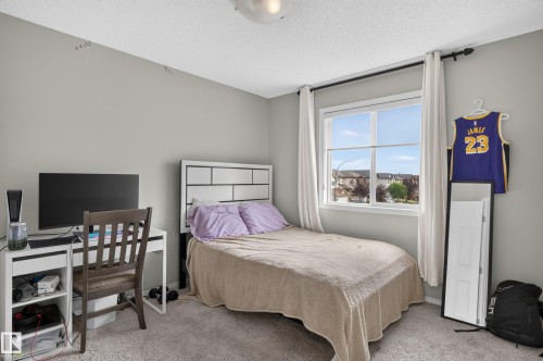 Neutral wall color, window with exterior streetscape, textured carpeting, and a white headboard - 17 Spruce Ridge Cove, Spruce Grove, AB - Indoor Photo Showing Bedroom
