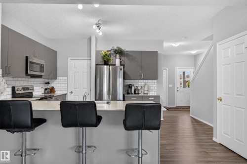 Open-concept kitchen featuring a peninsula with countertop seating, stainless steel appliances, a subway tile backsplash, and dark wood-finish flooring throughout - 17 Spruce Ridge Cove, Spruce Grove, AB - Indoor Photo Showing Kitchen With Upgraded Kitchen