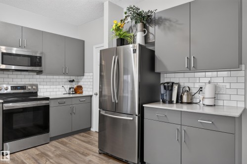 Kitchen featuring stainless steel appliances, white subway tile backsplash, light-toned countertops, gray cabinetry, and wood-finish flooring - 17 Spruce Ridge Cove, Spruce Grove, AB - Indoor Photo Showing Kitchen With Upgraded Kitchen