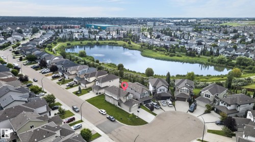 Aerial view showcasing this residential community featuring tree-lined streets, manicured lawns, and modern single-family homes with varied architectural styles - 17 Spruce Ridge Cove, Spruce Grove, AB - Outdoor With Body Of Water With View