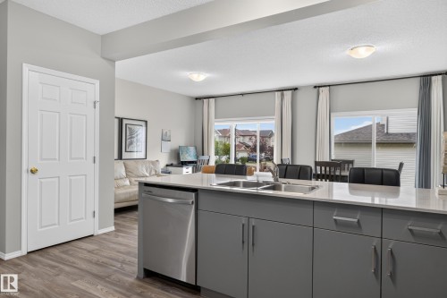 Modern kitchen featuring a large island with waterfall-edge countertop, stainless steel dishwasher, and gray cabinetry with integrated hardware - 17 Spruce Ridge Cove, Spruce Grove, AB - Indoor Photo Showing Kitchen With Double Sink