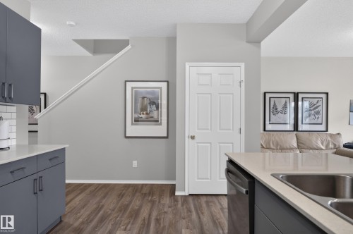 Modern kitchen and open living area featuring stainless steel appliances, white six-panel closet doors, dark cabinetry with brushed metal hardware, wood-finish flooring throughout, and recessed ceiling lighting - 17 Spruce Ridge Cove, Spruce Grove, AB - Indoor Photo Showing Kitchen