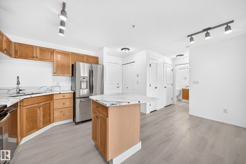 Kitchen featuring wood cabinetry, white countertops, stainless steel refrigerator, and an island - #214 245 Edwards Dr Sw, Edmonton, AB - Indoor Photo Showing Kitchen