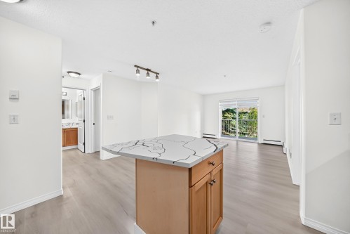 Kitchen island with a patterned countertop and wood-finish cabinetry - #214 245 Edwards Dr Sw, Edmonton, AB - Indoor Photo Showing Other Room