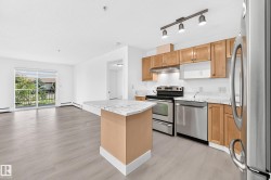 Open-concept living area featuring light wood-finish flooring, white walls, and a kitchen island with a waterfall countertop - 