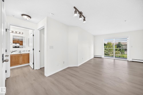 Open-concept living area with light-toned wood-finish flooring and white baseboards - #214 245 Edwards Dr Sw, Edmonton, AB - Indoor