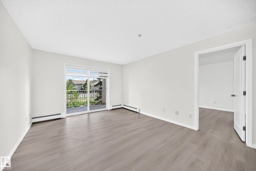 Spacious room featuring wood-finish flooring, white baseboards, and light-toned walls - #214 245 Edwards Dr Sw, Edmonton, AB - Indoor Photo Showing Other Room