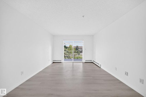 Spacious room featuring light wood-finish flooring, white baseboards, and a sliding glass door leading to a private balcony - #214 245 Edwards Dr Sw, Edmonton, AB - Indoor