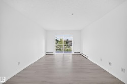 Spacious room featuring light wood-finish flooring, white baseboards, and a sliding glass door leading to a private balcony - 