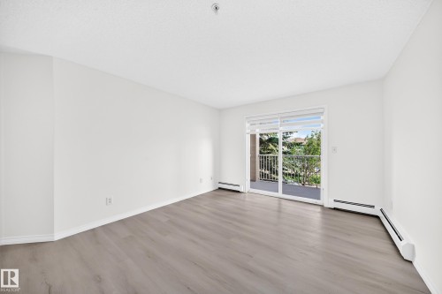 Spacious room featuring wood-finish flooring, white baseboards, and bright white walls - #214 245 Edwards Dr Sw, Edmonton, AB - Indoor