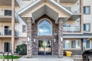 Building entrance featuring stone columns, glass double doors, an arched transom window, and a prominent building sign - #214 245 Edwards Dr Sw, Edmonton, AB  - Outdoor With Balcony With Facade 