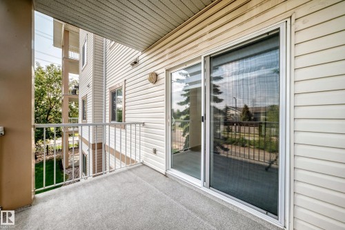 Private balcony featuring durable outdoor carpeting, white metal railing, and a sliding glass door with an integrated screen - #214 245 Edwards Dr Sw, Edmonton, AB - Outdoor With Balcony With Exterior