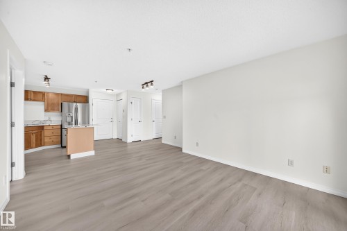 Open-concept living area featuring wood-finish flooring, light neutral walls, recessed lighting, and a kitchen with stainless steel appliances, wood cabinetry, and a central island - #214 245 Edwards Dr Sw, Edmonton, AB - Indoor