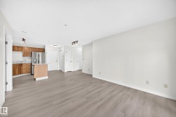 Open-concept living area featuring wood-finish flooring, light neutral walls, recessed lighting, and a kitchen with stainless steel appliances, wood cabinetry, and a central island - 