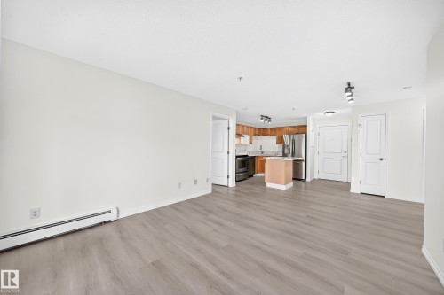 Open-concept living space featuring wood-finish flooring, white walls, and track lighting - #214 245 Edwards Dr Sw, Edmonton, AB - Indoor