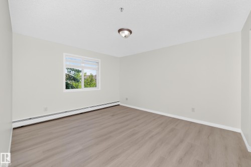 Bright room featuring light wood-finish flooring, a contemporary ceiling light fixture, and a window with white trim - #214 245 Edwards Dr Sw, Edmonton, AB - Indoor Photo Showing Other Room