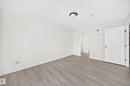 Spacious interior room featuring light wood-finish flooring, white baseboards, and white walls - #214 245 Edwards Dr Sw, Edmonton, AB - Indoor Photo Showing Other Room