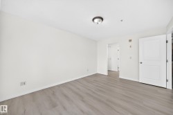 Spacious interior room featuring light wood-finish flooring, white baseboards, and white walls - 